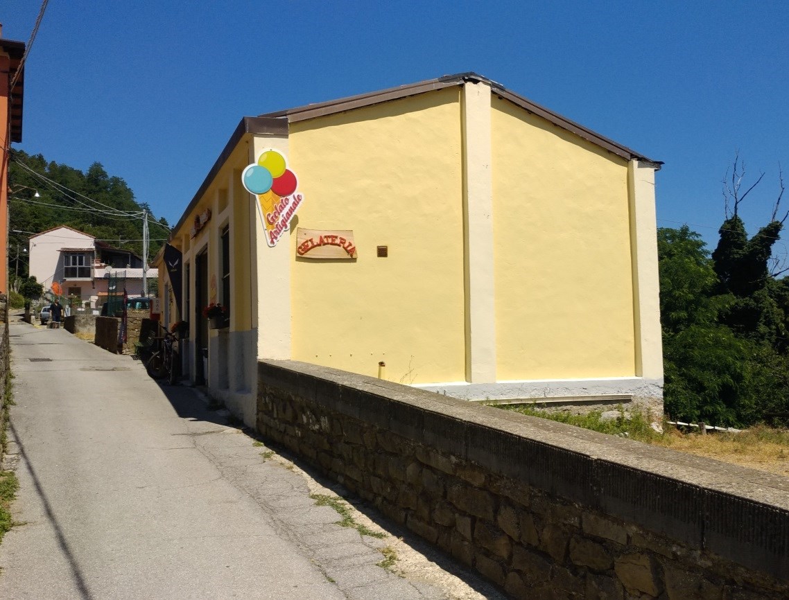 Il fabbricato, di forma planimetrica rettangolare, è disposto su unico piano fuori terra, avente ampio fronte sulla strada carrabile; è composto da un ampio locale disposto su due livelli sfalsati di circa m 0,70, dotato di servizio igienico, già destinato ad attività commerciale, avente superficie complessiva, rilevata al lordo delle murature, di circa mq 97 ed altezze interne di m 3,30 e m 2,60. E’ pertinenziale al fabbricato tratto di corte della superficie di circa mq 17, in gran parte occupata dalla sede stradale della Via della Chiesa ed in piccola parte sterrata. Corte m² 17. Sup. 84 m²