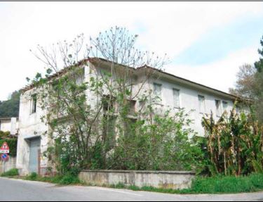 L’edificio in totale abbandono. Al piano terra una unità immobiliare con accesso dall’ingresso comune con le due unità abitative, composta da quattro vani per ufficio, due servizi igienici e corridoio suddiviso in due distinte porzioni.  Al piano terreno nella parte ovest un unico locale a pianta rettangolare utilizzata come rimessa. Il piano primo, cui si perviene mediante ingresso e scala interna a comune, è costituito da due unità immobiliari ad uso residenziale disabitate da 10 anni. L’appartamento sul lato est, dotato anche di accesso autonomo dallo stradello retrostante, si compone di tre vani, cucina, corridoio e servizio igienico. L’appartamento sul lato ovest si compone di tre vani, cucina, servizio igienico e corridoio, e piccolo ripostiglio sottoscala situato al piano terreno.