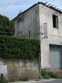 L’edificio in totale abbandono. Al piano terra una unità immobiliare con accesso dall’ingresso comune con le due unità abitative, composta da quattro vani per ufficio, due servizi igienici e corridoio suddiviso in due distinte porzioni.  Al piano terreno nella parte ovest un unico locale a pianta rettangolare utilizzata come rimessa. Il piano primo, cui si perviene mediante ingresso e scala interna a comune, è costituito da due unità immobiliari ad uso residenziale disabitate da 10 anni. L’appartamento sul lato est, dotato anche di accesso autonomo dallo stradello retrostante, si compone di tre vani, cucina, corridoio e servizio igienico. L’appartamento sul lato ovest si compone di tre vani, cucina, servizio igienico e corridoio, e piccolo ripostiglio sottoscala situato al piano terreno.