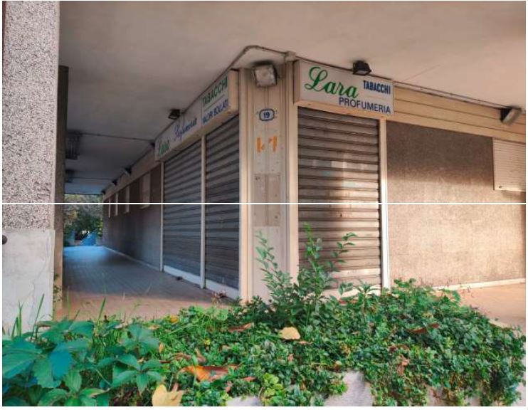 L'unità immobiliare si affaccia sulla via Tirana e, anche se posta al piano terra del fabbricato si trova ad un livello rialzato rispetto al piano stradale. L'unità ha una superficie commerciale di mq 70 ed è composta da un locale principale adibito a negozio, un wc e un locale destinato a retro-negozio, con un'altezza dei locali di m. 3,00. ID Cat. [N.C.E.U.] Unità Commerciale cat.C/1 Foglio 85 (ex B/13) part. 479 (ex 1308) sub 2. Sup mq 70 catastali. Lotto libero, piena proprietà.